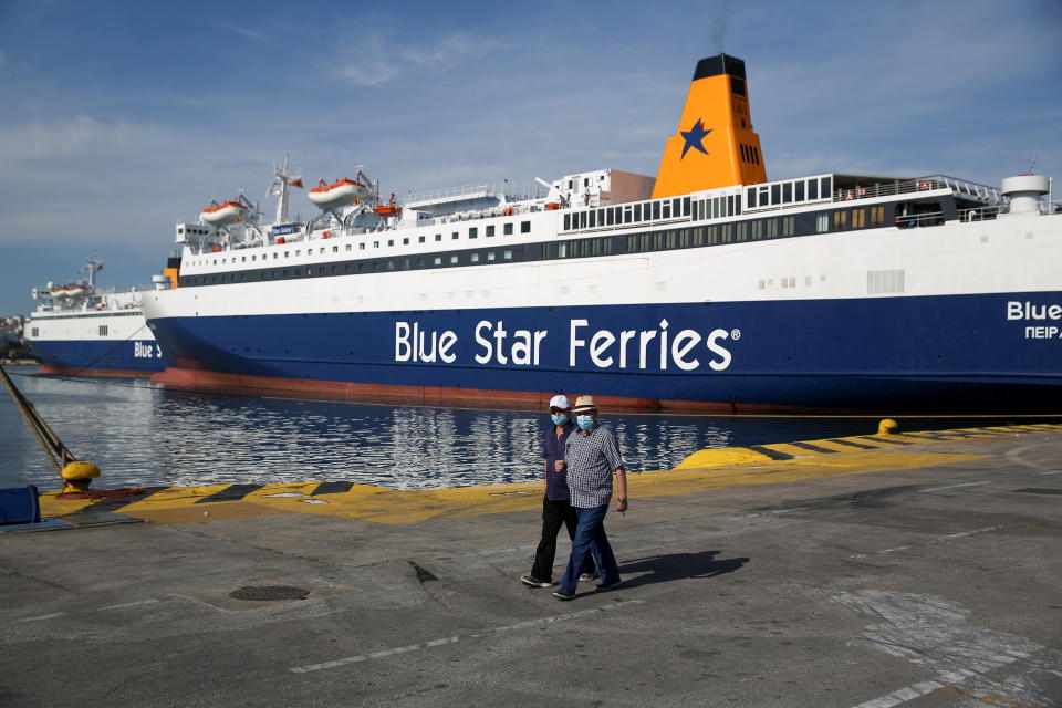 People walk next to a moored passenger ferry during a 24-hour general strike at the port of Piraeus