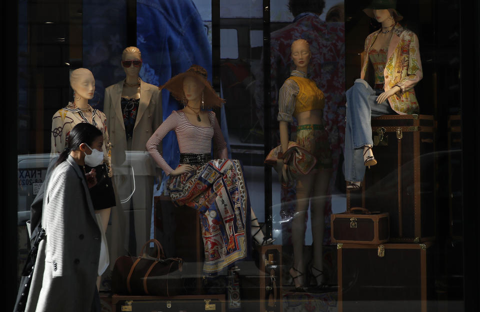 A woman wearing a face mask walks past a fashion store's front window in Monte Napoleone shopping street during the Fashion Week, in Milan, Italy, Wednesday, Feb. 24, 2021. (AP Photo/Antonio Calanni)