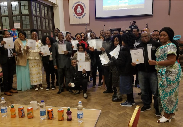 A group of people stand in a hall holding up pieces of paper.