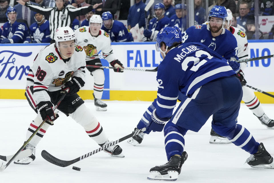 Chicago Blackhawks center Connor Bedard (98) tries to get past Toronto Maple Leafs defenseman Jake McCabe (22) during third-period NHL hockey game action in Toronto, Monday, Oct. 16, 2023. (Nathan Denette/The Canadian Press via AP)