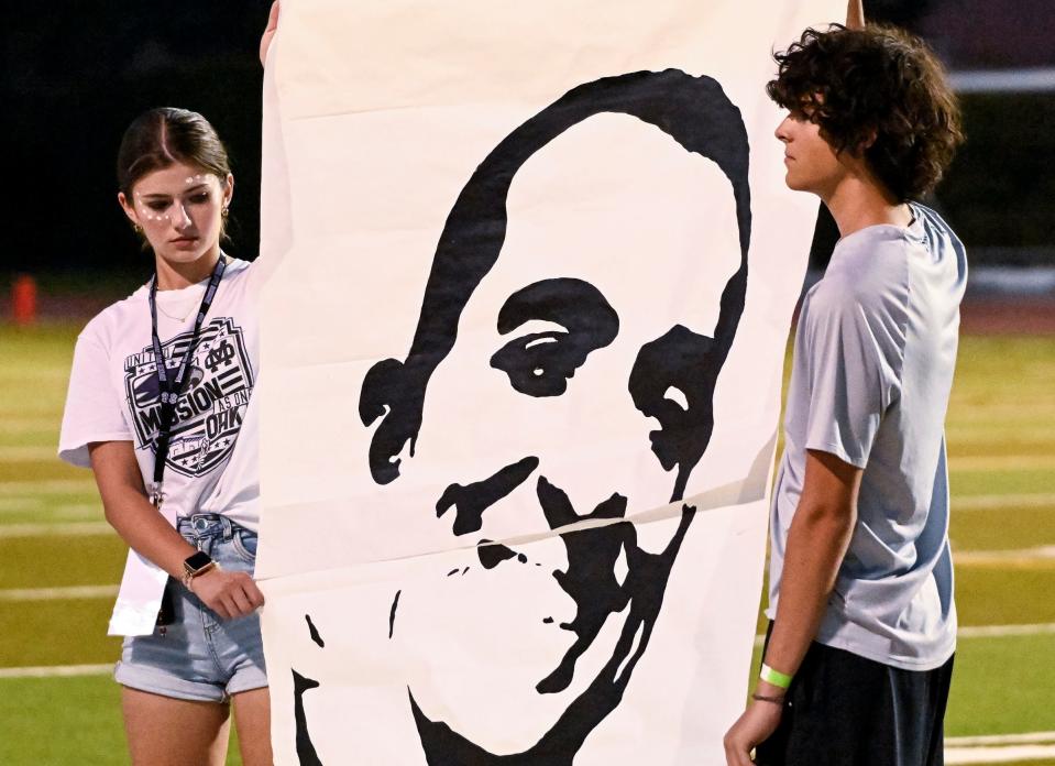 Mission Oak students hold a picture of former teacher Mike Hazelwood on Thursday, August 17, 2023 during a moment of silence in his honor before the football game against Monache. Hazelwood died unexpectedly from heart complications on May 18.