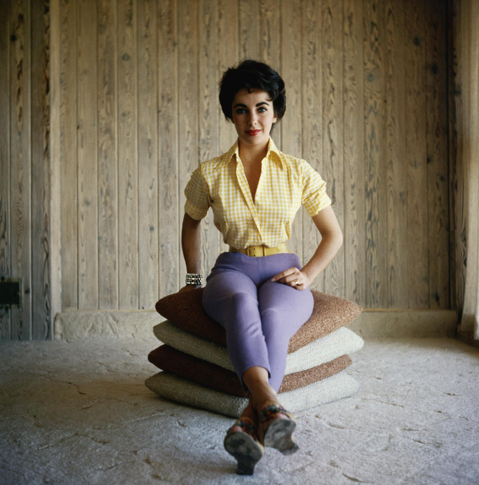 Actress Elizabeth Taylor sits on a stack of pillows, wearing purple pants and a yellow shirt in this undated photo.&nbsp;