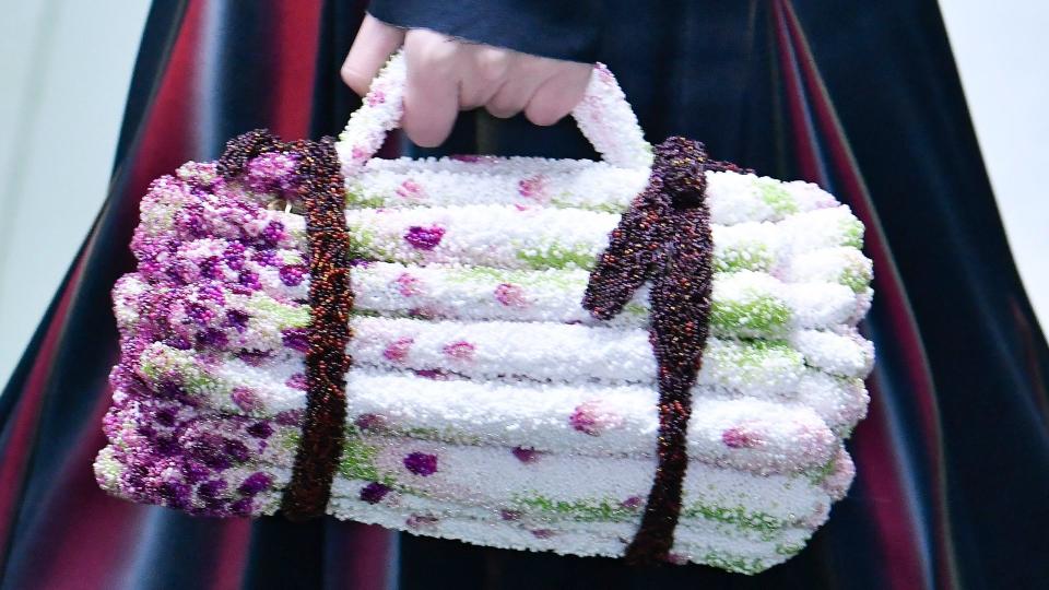 A model walks the runway during the Loewe Ready to Wear Fall/Winter 2024-2025 holding a bag that looks like a bunch of asparagus 