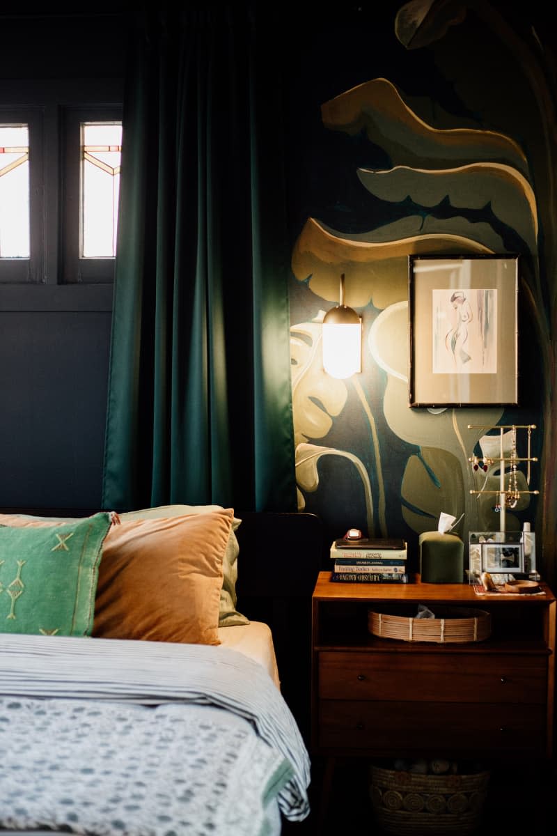 bedroom with dark colored walls with plant leaves painted, dark green curtains, windows with stained glass accents