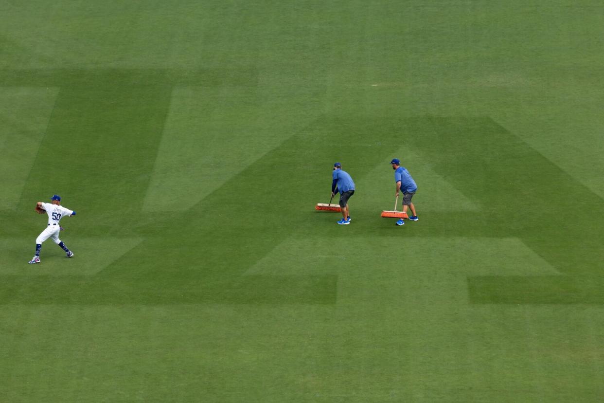 Los Angeles Dodgers' Mookie Betts warms up as the grounds crew work on the outfield.