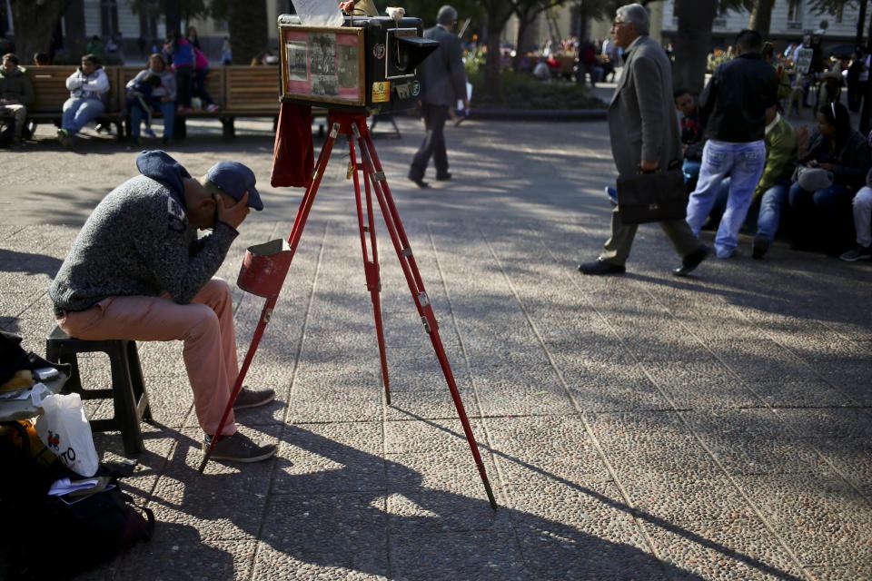 En esta imagen del 1 de septiembre de 2016, el fotógrafo Luis Maldonado espera a que lleguen clientes junto a su vieja cámara de cajón en la Plaza de Armas de Santiago de Chile. Pueden pasar días y hasta semanas hasta que alguien le pida un retrato. (AP Foto/Esteban Félix)