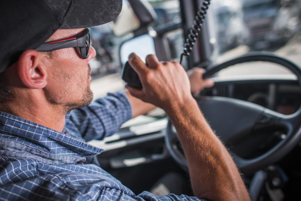 Caucasian Truck Driver in his 30s CB Talking with Other Drivers in the Convoy. Heavy Load Transportation Communication.