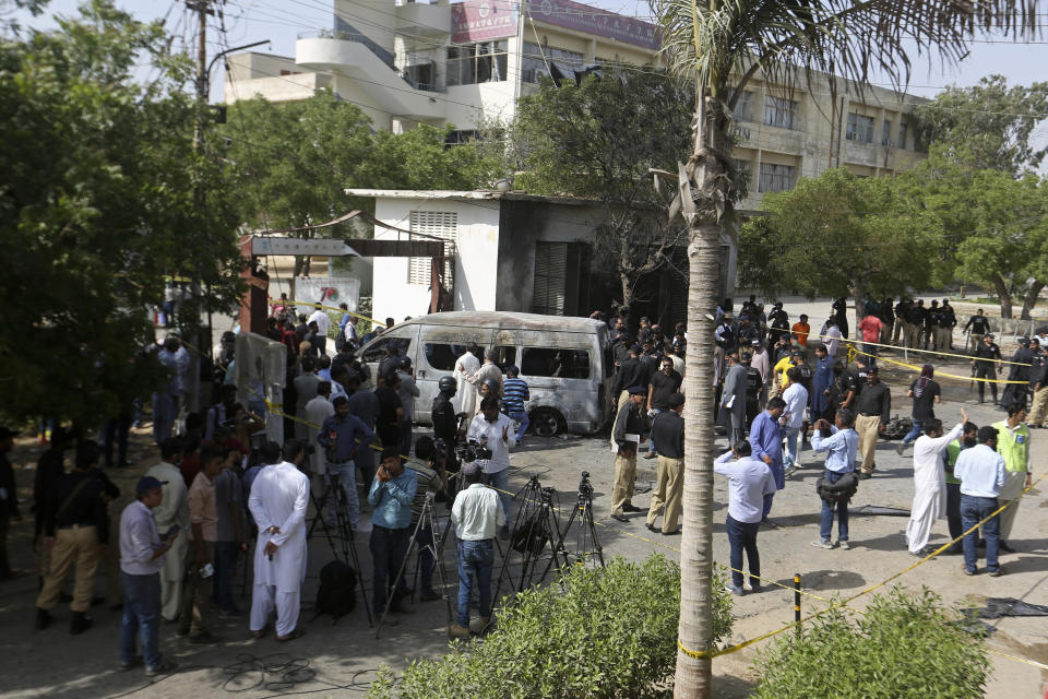Pakistani police officers and journalists gather near a burned van at the site of an explosion, in Karachi, Pakistan, Tuesday, April 26, 2022. The explosion ripped through a van inside a university campus in southern Pakistan on Tuesday, killing several people including Chinese nationals and their Pakistani driver, officials said. (AP Photo/Fareed Khan)