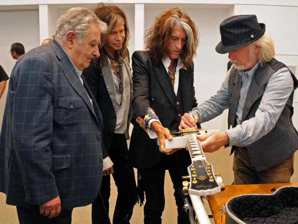 In this picture released by Uruguay's Press Office, Uruguay's president Jose Mujica, left, watches Aerosmith's band members Steven Tyler, second from left, Joe Perry, second from right, and Brad Whitford autograph a guitar he received as a gift at the presidential house in Montevideo, Uruguay, Tuesday, Oct. 8, 2013. The band will perform Wednesday as part of their Latin America tour. (AP Photo/Uruguay Press Office, Alvaro Salas)