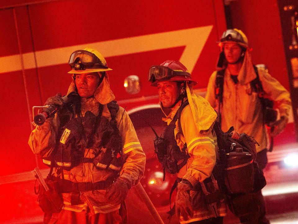 Firefighters watch a fire in front of a fire truck.