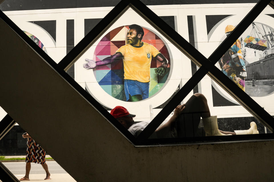 A man rests in front of a mural with an image of soccer legend Pele, created by Brazilian street artist Eduardo Kobra in Santos, Brazil, Monday, Dec. 26, 2022. (AP Photo/Matias Delacroix)