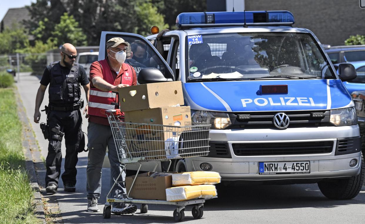 Helpers bring food to families behind a fence, who are quarantined in their apartments in Verl, Germany, Tuesday, June 23, 2020. Following the corona outbreak at meat processor Toennies in Rheda-Wiedenbrueck, the federal state authorities are massively restricting public life in the Guetersloh district with a lockdown. (AP Photo/Martin Meissner)