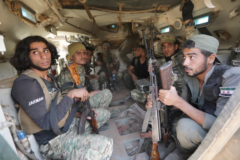 Turkey-backed Syrian rebel fighters ride in their military tank near the border town of Tal Abyad