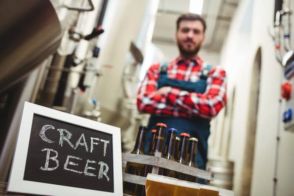 Craft brewer standing behind an 8-pack of beer, next to a small chalkboard reading CRAFT BEER