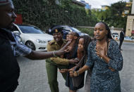 Civilians flee helped by a member of the security forces at a hotel complex in Nairobi, Kenya, Tuesday, Jan. 15, 2019. Terrorists attacked an upscale hotel complex in Kenya's capital Tuesday, sending people fleeing in panic as explosions and heavy gunfire reverberated through the neighborhood. (AP Photo/Ben Curtis)