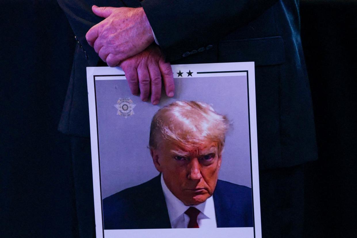 <span>A person holds a placard with Donald Trump’s mugshot at a rally in Durham, New Hampshire, on 16 December 2023.</span><span>Photograph: Brian Snyder/Reuters</span>