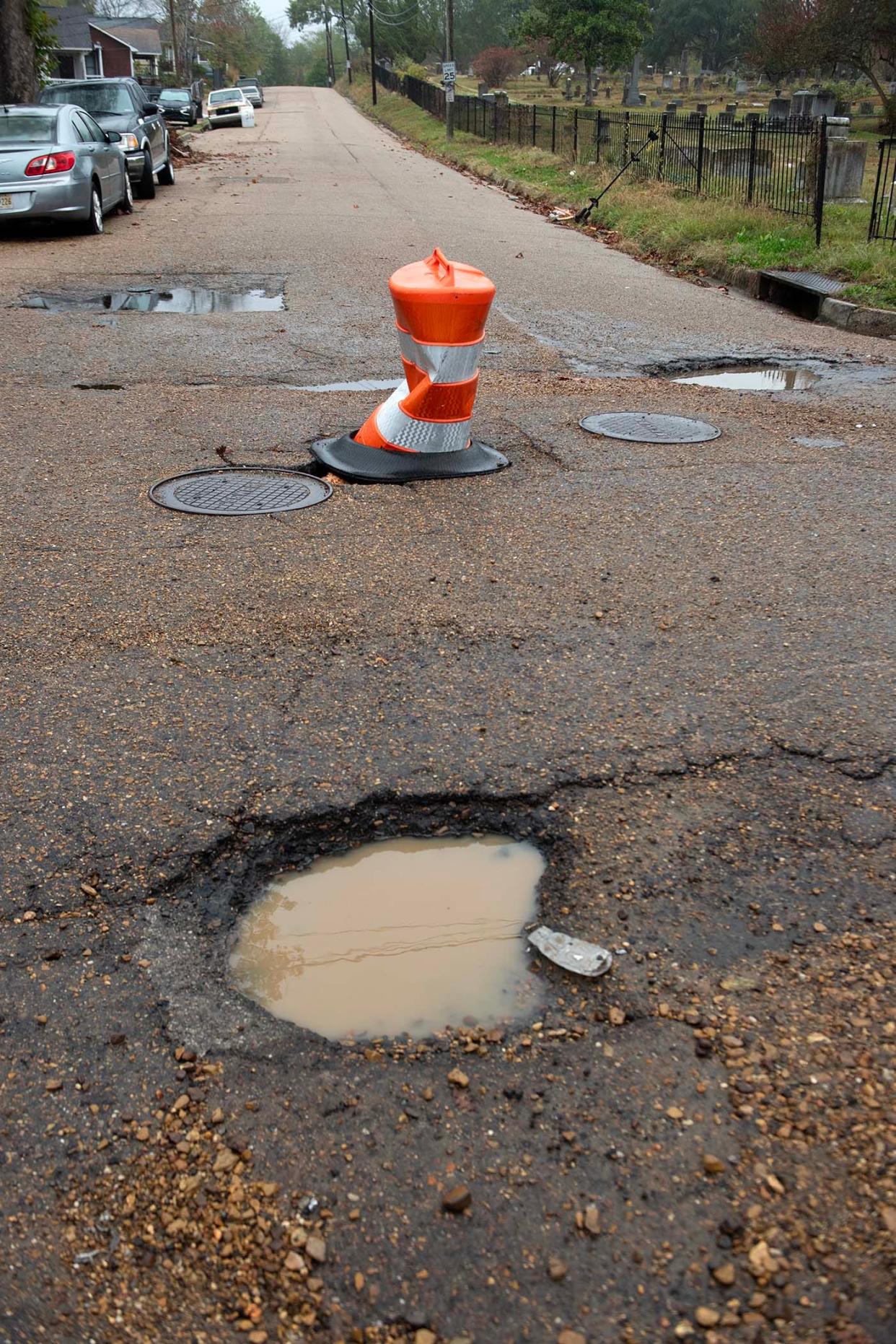 A traffic barrel covering a pothole at Lamar Street in Jackson is surrounded by other potholes at the intersection of North Lamar and Davis Streets Tuesday, Nov. 21, 2023.