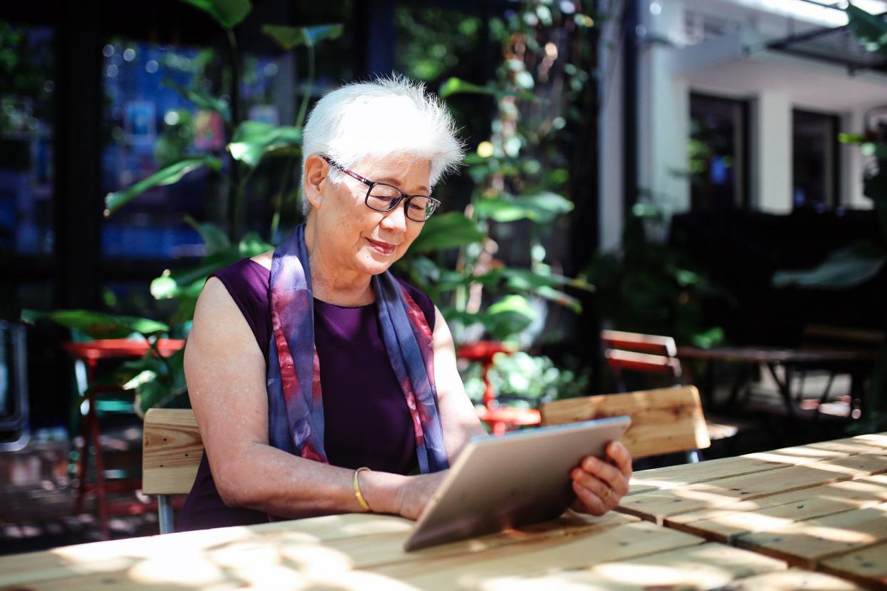 senior woman using tablet, seated at outdoor table