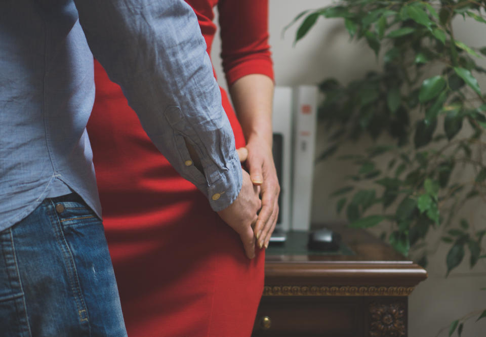 A person in a blue shirt and jeans places their hand gently on a person in a red dress, creating an intimate moment