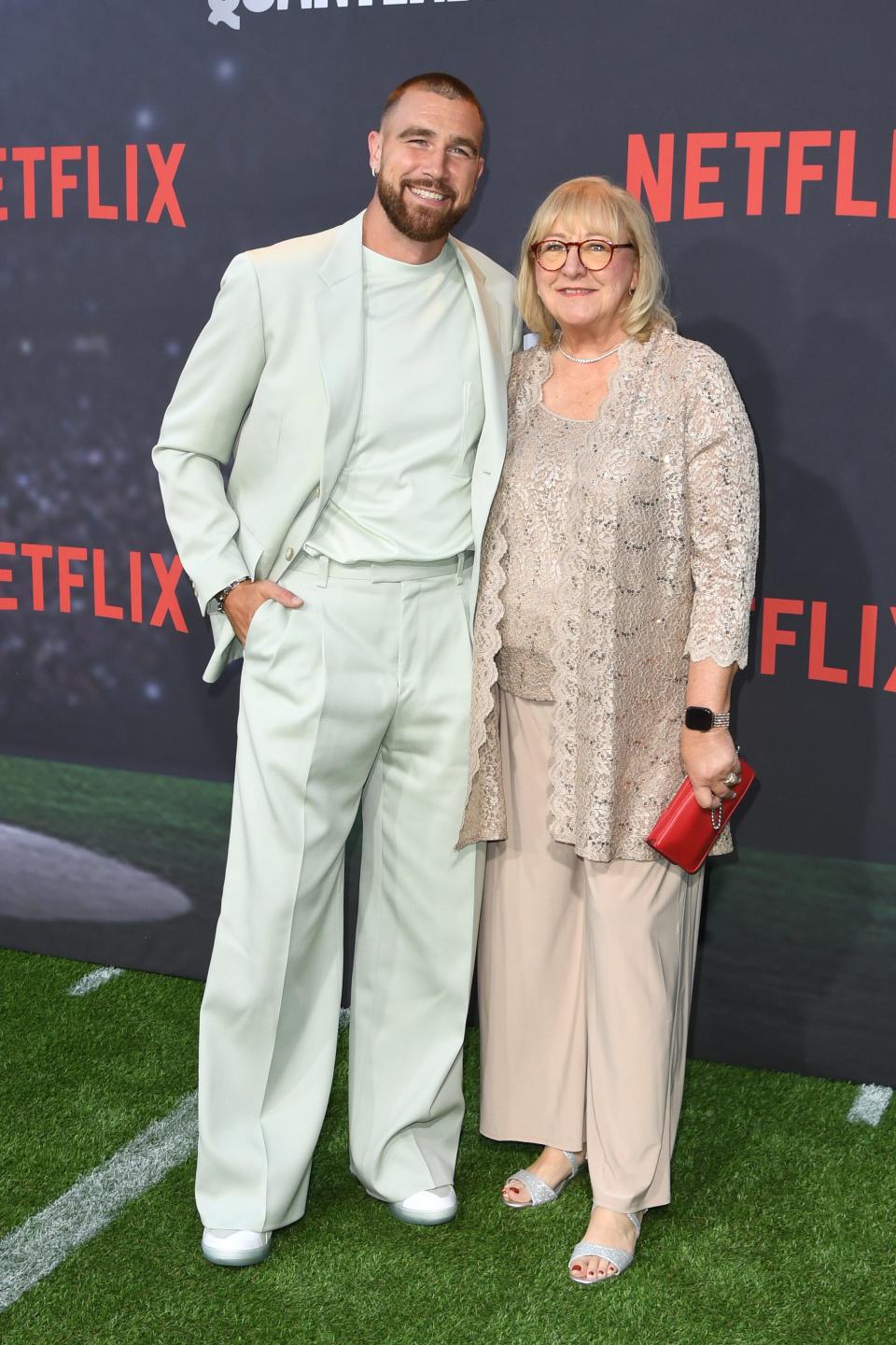 Travis Kelce wearing a mint green suit next to his mother Donna Kelce, who is wearing a beige outfit.