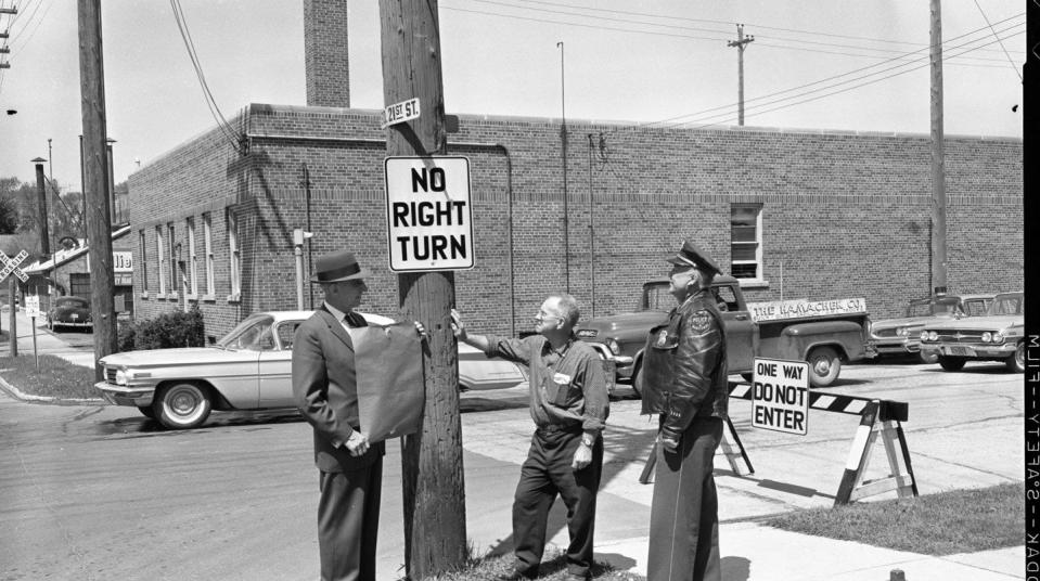 Chief Frank Tomchek, Ald. Charles Cizek and Traffic Lt. Melvin Reinhardt at the corner of South 21st and Franklin streets removing the covering from the “No Right Turn” sign. In the background is a barricade preventing traffic from going eastbound on Franklin Street.