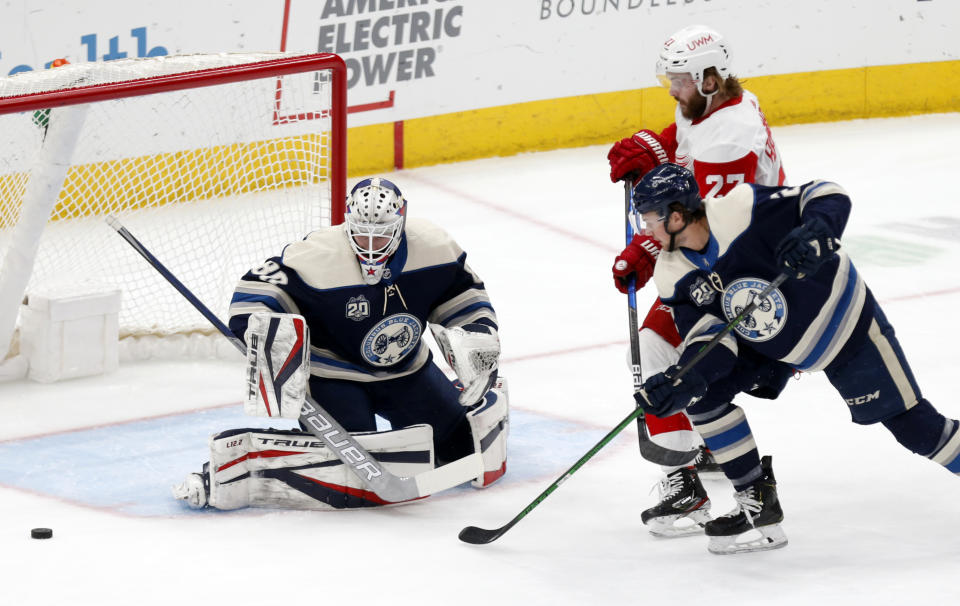 Columbus Blue Jackets goalie Elvis Merzlikins, left, stops a shot by Detroit Red Wings forward Michael Rasmussen, right, as Blue Jackets' Andrew Peeke defends during the first period of an NHL hockey game in Columbus, Ohio, Friday, May 7, 2021. (AP Photo/Paul Vernon)