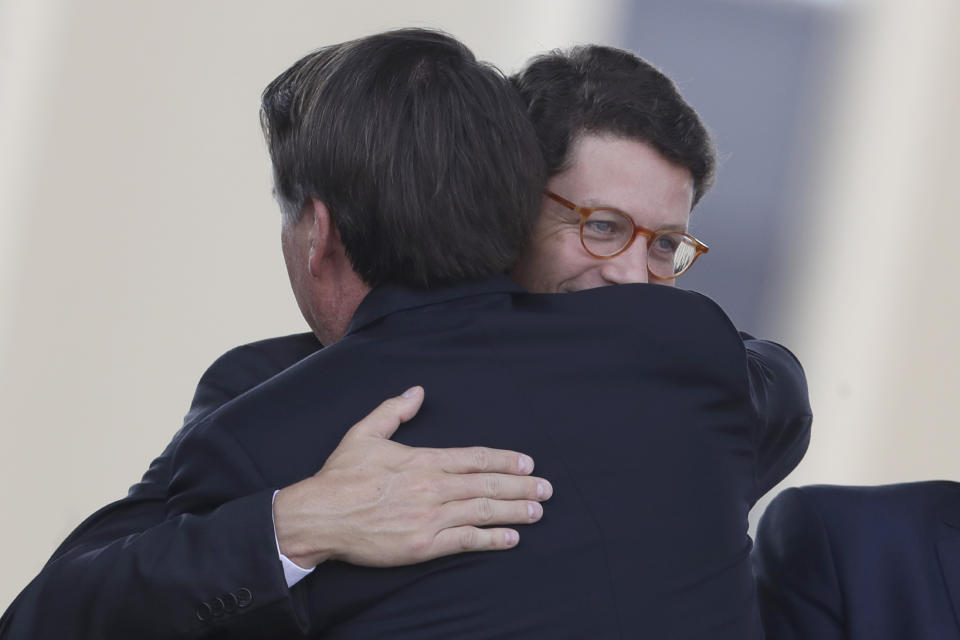 FILE - In this Aug. 23, 2019 file photo, Brazilian President Jair Bolsonaro, back, embraces his Environment Minister Ricardo Salles during a military ceremony for the Day of the Soldier at the army headquarters in Brasilia, Brazil. Amidst a broader government effort to slash public spending, Salles announced in April a 24% budget cut for Ibama, the government’s Brazilian Institute of the Environment and Renewable Natural Resource, which carries out on-the-ground operations tackling environmental crime in hot spots identified through a mix of intelligence and satellite images. (AP Photo/Eraldo Peres, File)