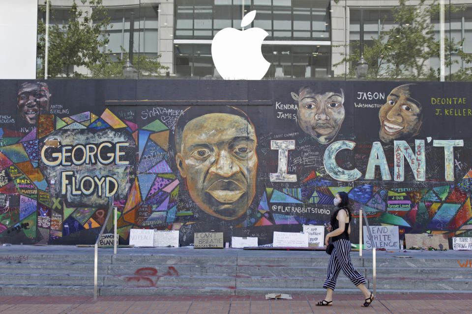 FILE - In this July 13, 2020, file photo, a pedestrian walks past a boarded-up Apple store that's been covered in street art in downtown Portland, Ore. A year after Portland's police department underwent significant budget cuts amid demands to defund the police, the city is looking to spend more than $5 million for police investments, including hiring more officers and buying body-worn cameras. (AP Photo/Gillian Flaccus, File)