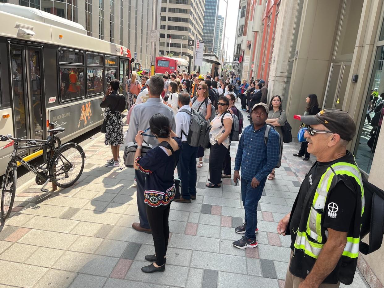 Afternoon commuters line up to catch R1 replacement buses on Queen Street in downtown Ottawa on July 18, 2023, due to a bearing-related shutdown of the entire Confederation Line. (Kristy Nease/CBC - image credit)