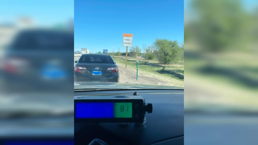 A car pulled over by a fines double sign. A device shows the driver was going 81 mph
