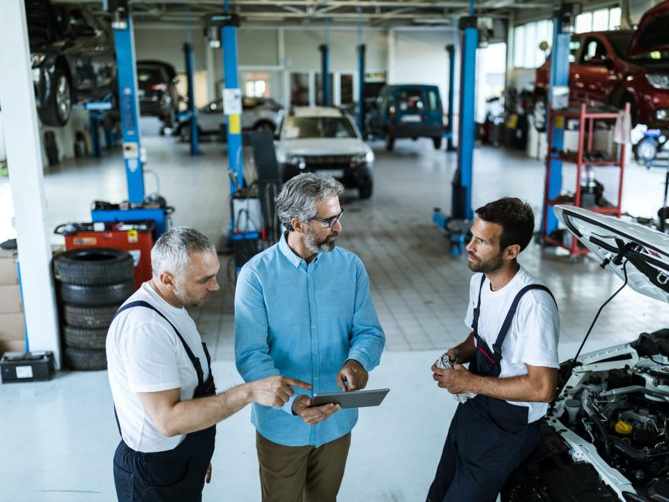 Manager using digital tablet while talking to mechanics in auto repair shop