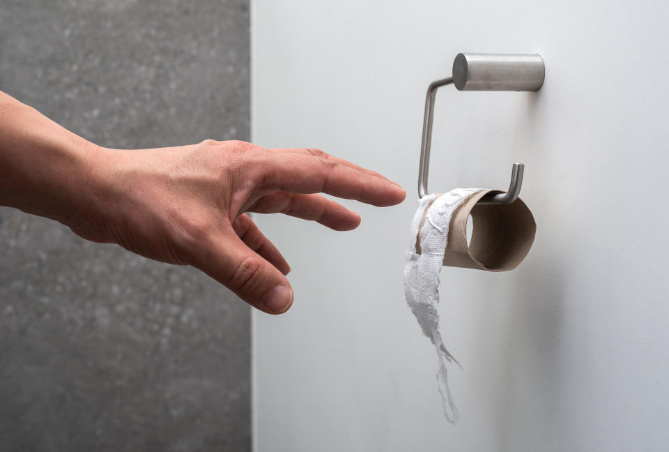 Eine Hand langt nach Toilettenpapier - die Rolle ist leer. 