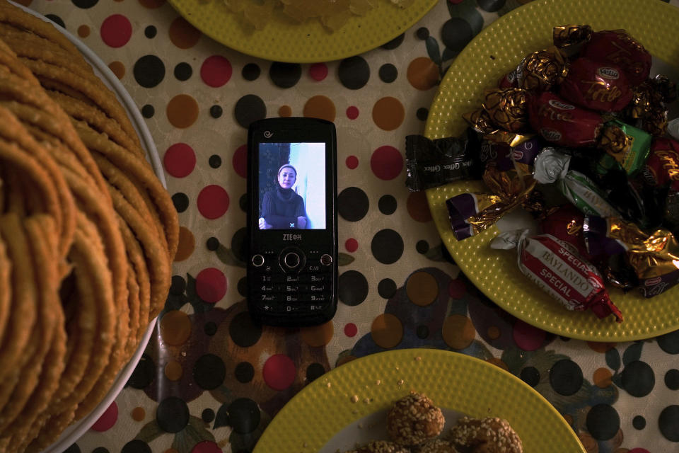 In this Aug. 24, 2018, photo, a phone displaying an image of Gulzar Seley, who was detained in China along with her newborn son, is placed on a table next to platters of sweets in the home of her husband Halmurat Idris in Istanbul, Turkey. Seley went back to China from Turkey two years ago to see her dying mother despite news of Uighurs being taken to reeducation and pleas from her husband for her not to go. She was detained upon landing in Urumqi, China, and Idris heard she was eventually imprisoned along with their son. (AP Photo/Dake Kang)