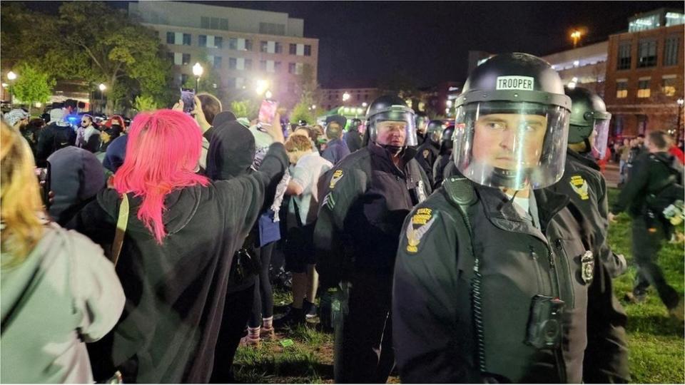 Police in riot gear, protesters holding phones