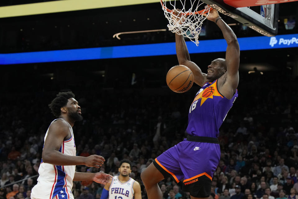 Phoenix Suns center Bismack Biyombo dunks next to Philadelphia 76ers center Joel Embiid and forward Tobias Harris (12) during the second half of an NBA basketball game Saturday, March 25, 2023, in Phoenix. The Suns won 125-105. (AP Photo/Rick Scuteri)