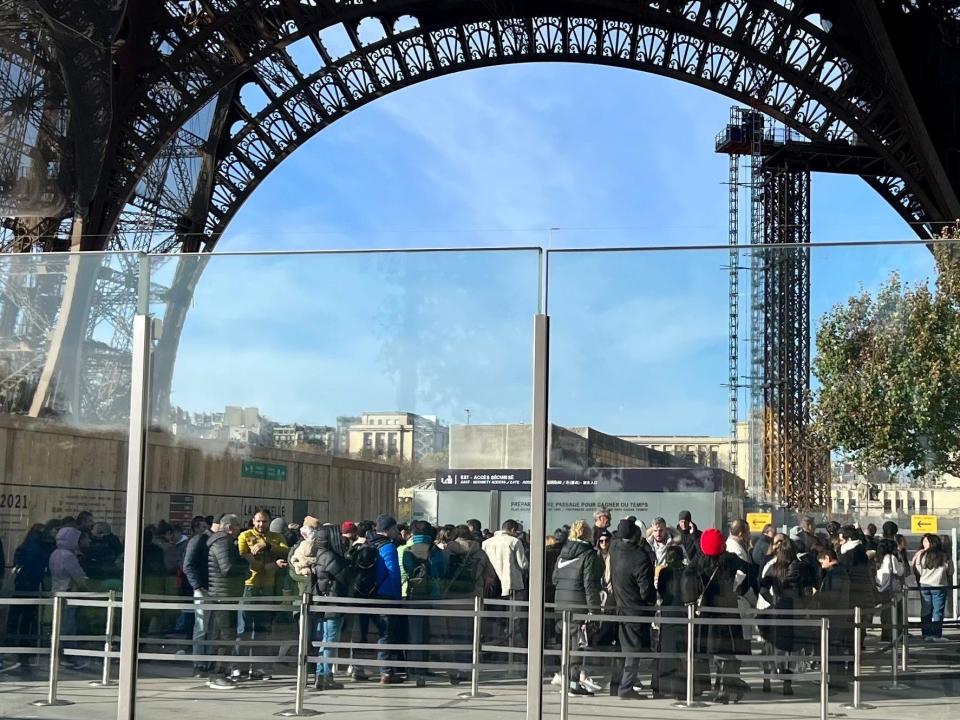 A glass wall separates people queueing to go up the Eiffel Tower.