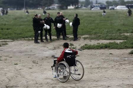 A refugee boy on a wheelchair passes in front of riot policemen during a police operation at a refugee camp at the border between Greece and Macedonia, near the village of Idomeni, Greece, 24 May 2016. REUTERS/Yannis Kolesidis/Pool