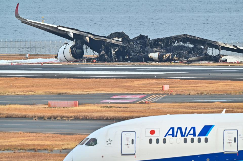 An All Nippon Airlines (ANA) plane taxis past the burnt wreckage of a Japan Airlines (JAL) passenger plane on the tarmac at Tokyo International Airport at Haneda in Tokyo on January 3, 2024, the morning after the JAL airliner hit a smaller coast guard plane on the ground.