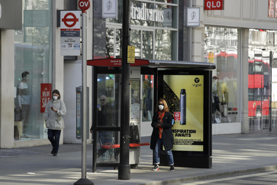 A masked woman waits at a bus stop on a deserted Oxford Street in London, Tuesday, March 24, 2020. Britain's Prime Minister Boris Johnson on Monday imposed its most draconian peacetime restrictions due to the spread of the coronavirus on businesses and gatherings, health workers begged for more gear, saying they felt like "cannon fodder." For most people, the new coronavirus causes only mild or moderate symptoms. For some it can cause more severe illness. (AP Photo/Matt Dunham)