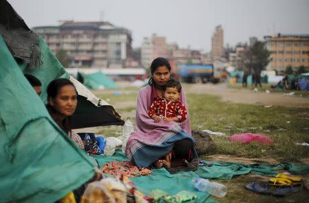 An earthquake victim holds her daughter as she sits outside her makeshift shelter on open ground in the early hours in Kathmandu, Nepal April 28, 2015. REUTERS/Adnan Abidi