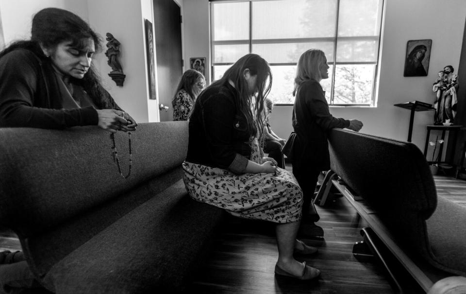 Women sit on pews and kneel to pray in a chapel