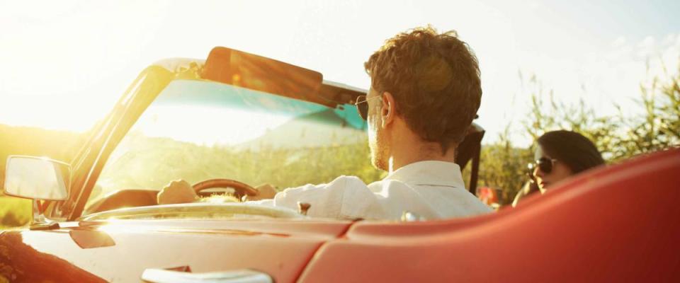 Couple driving convertible car enjoying a summer day at sunset