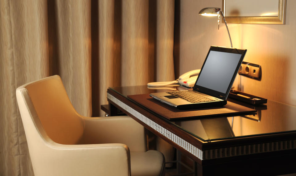 Laptop on hotel desk with chair, lamp, and notepad, representing a mobile work environment