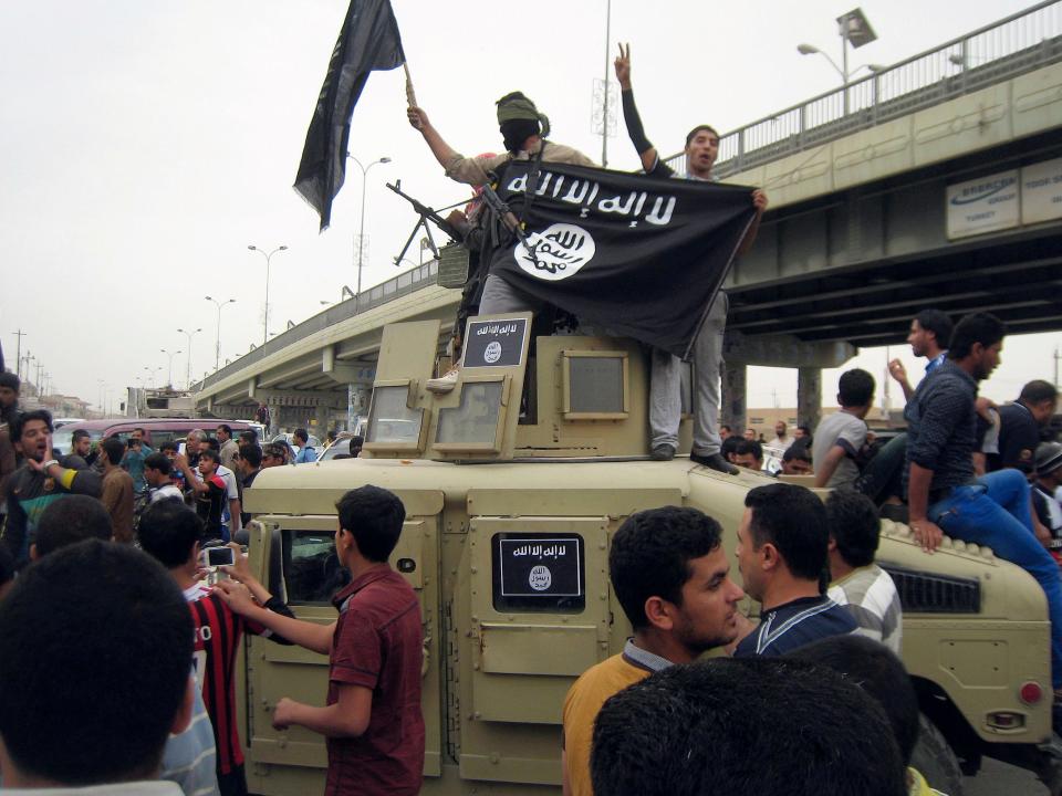 In this March 30, 2014 photo, Islamic State group militants hold up their flag as they patrol in a commandeered Iraqi military vehicle in Fallujah, Iraq.