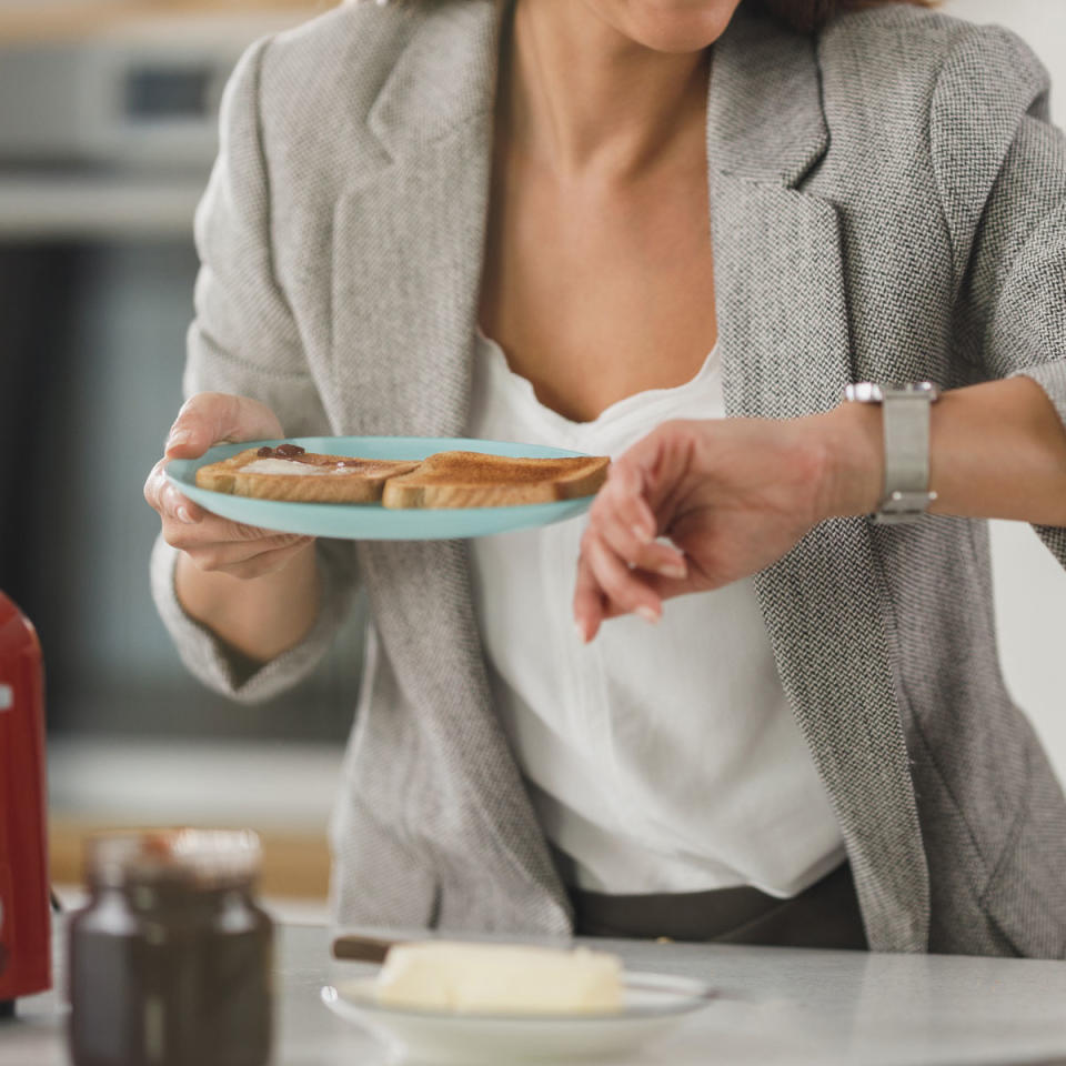 A woman holding a plate of toast and checking the clock