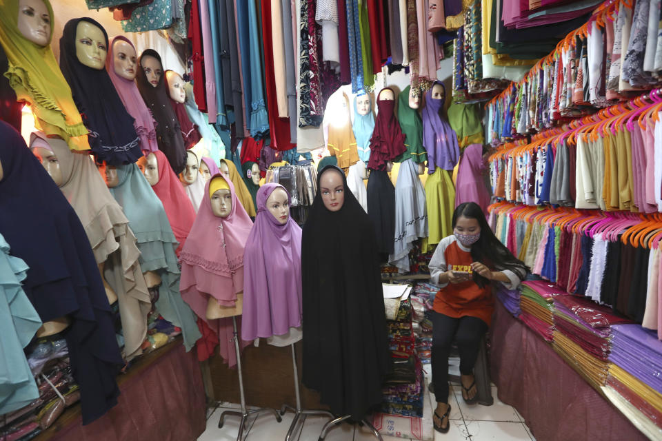 A head scarf vendor wearing a face mask waits for customers at a traditional market in Tangerang, Indonesia, Saturday, May 9, 2020. (AP Photo/Tatan Syuflana)