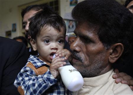 Nine-month-old baby Khan drinks milk from his bottle while being carried by his grandfather Muhammad Yasin as they leave after appearing in a court in Lahore