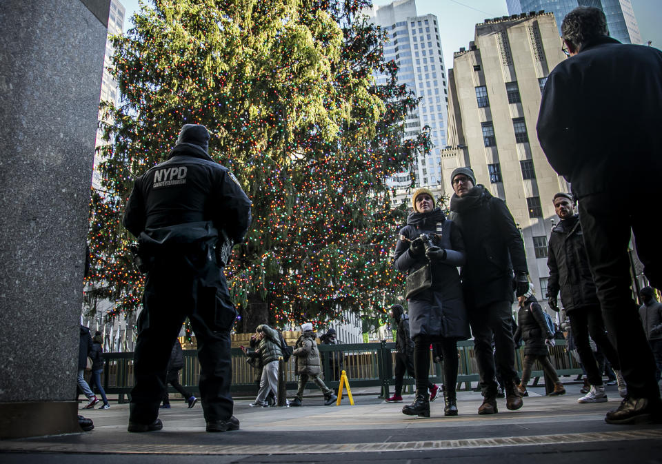 In this Thursday, Dec. 19, 2019 photo, an NYPD officer, left, patrols near the Christmas tree at Rockefeller Center, in New York. The area had seen a recent appearance of costumed performers soliciting money for photos, but unlike Times Square—where the city passed a law relegating the characters to 8-by-50 foot "activity zones," no such zones exist around Rockefeller Center and its iconic Christmas tree. (AP Photo/Bebeto Matthews)