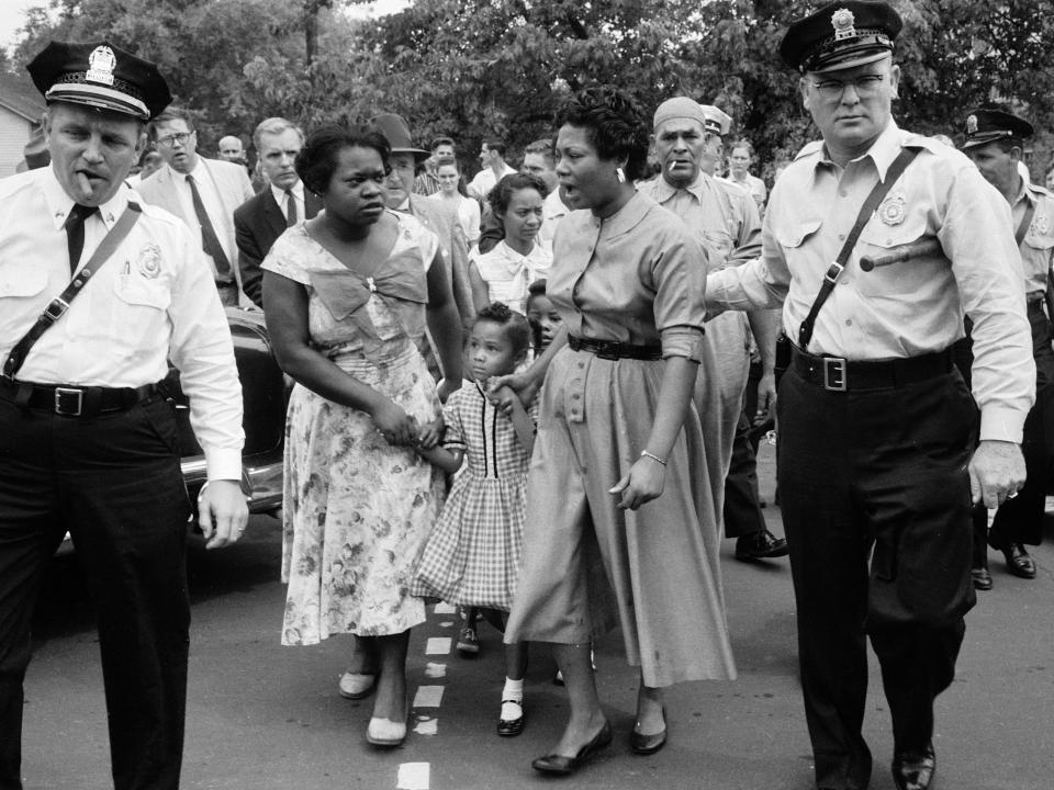 Police in Nashville escorting African American mothers with grade school kids past jeering mob of demonstrators after the desegregation of the school.