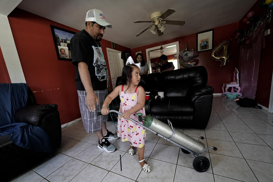 Melanii Fernandez, 4, puts a portable oxygen tank away after going for a walk with her father, Freddy Fernandez Friday, June 10, 2022, in Carthage, Mo. After contracting COVID-19 in August 2021, Fernandez spent months hooked up to a respirator and an ECMO machine before coming home in February 2022 to begin his long recovery from the disease. (AP Photo/Charlie Riedel)